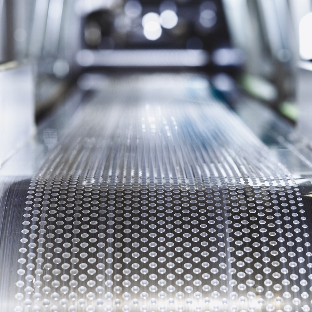 Close-up of a transparent plastic film with evenly spaced circular patterns on a production line in a manufacturing setting.